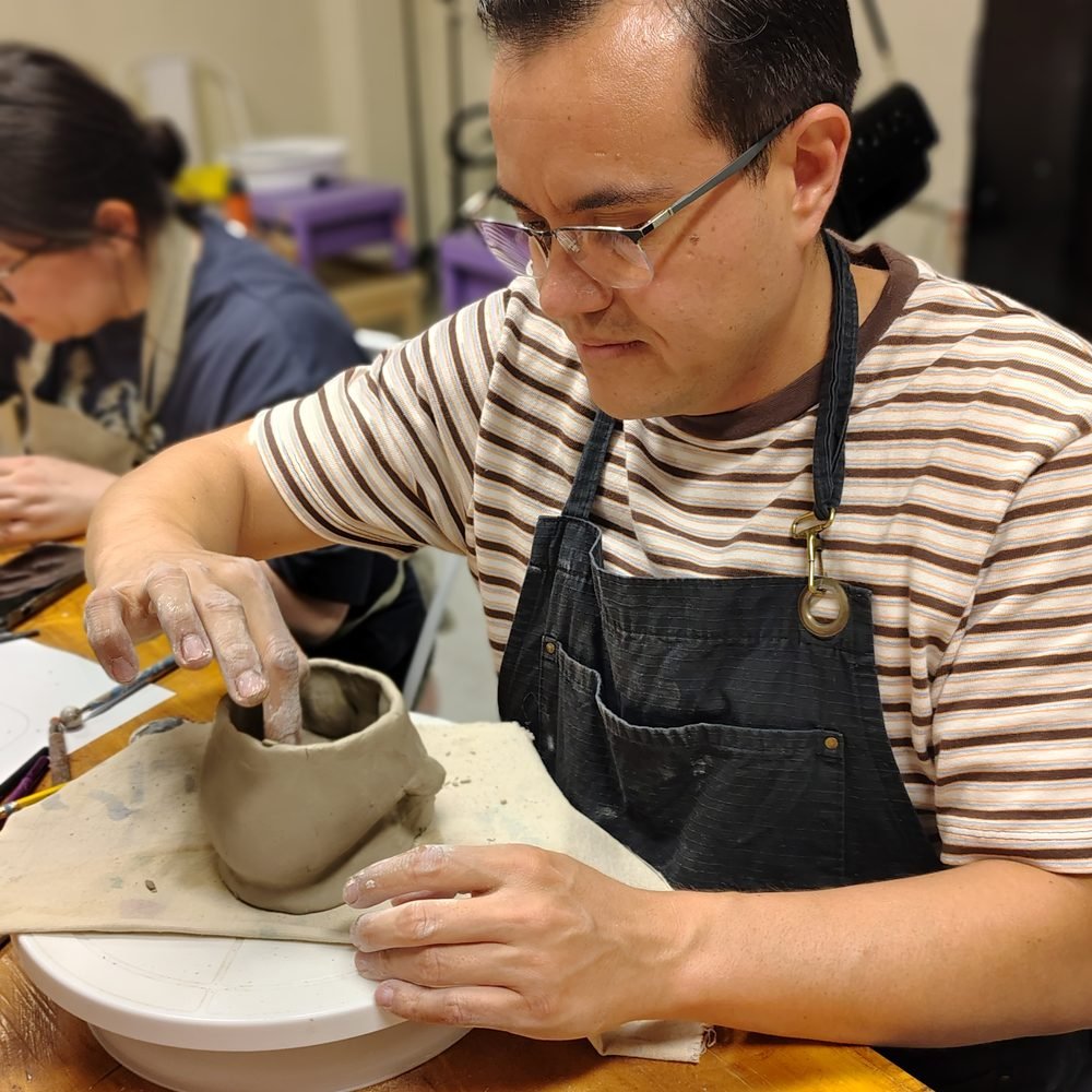 Participante con mandil modelando una taza de arcilla con las manos en el taller de cerámica