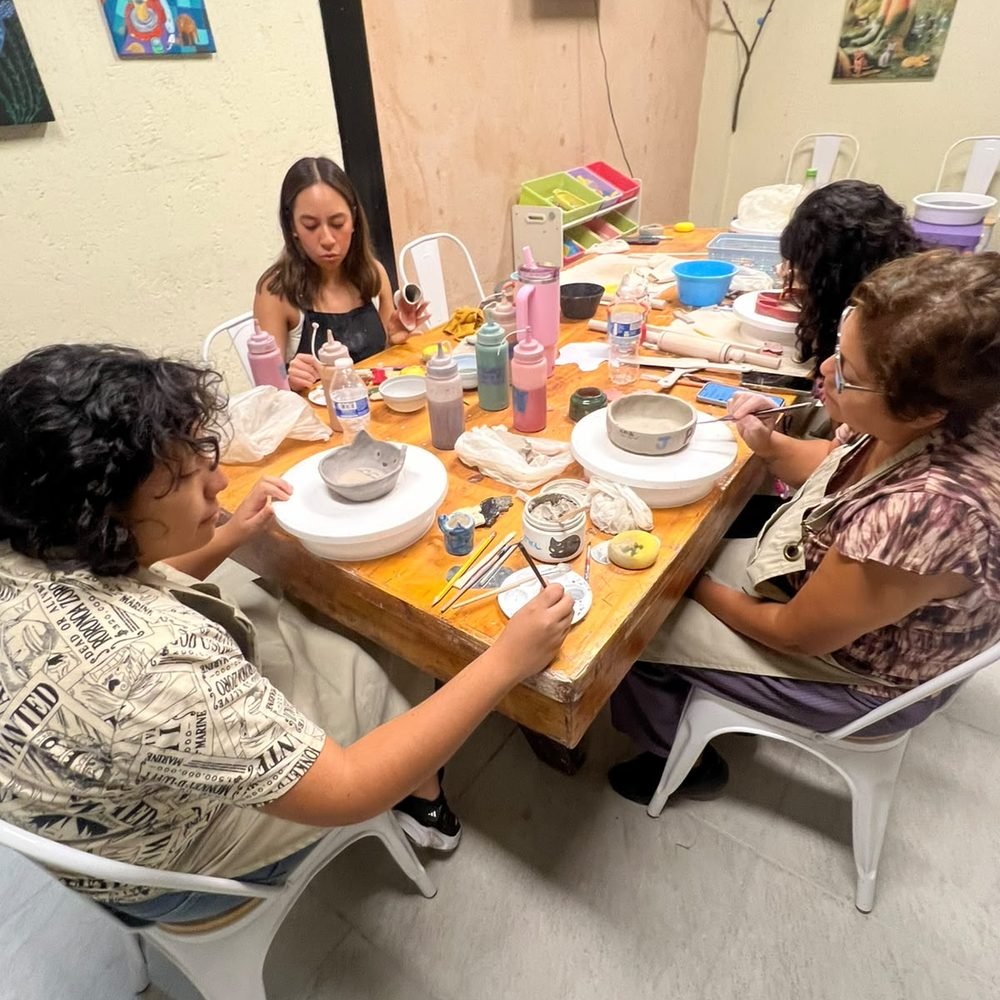 Grupo de adultos trabajando sus piezas alrededor de la mesa del taller de cerámica