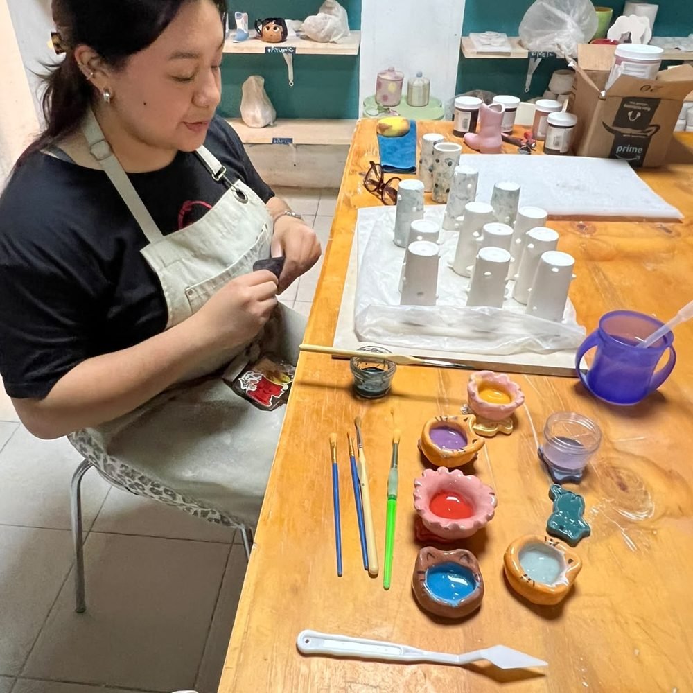 Participante decorando piezas de cerámica con engobes de colores en la mesa del taller