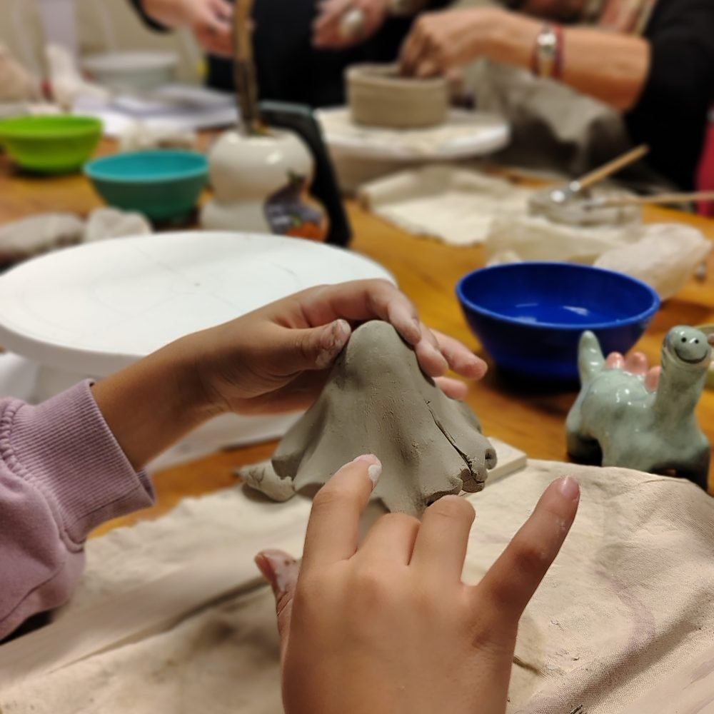 Manos de una niña modelando una figura de arcilla en el taller de cerámica