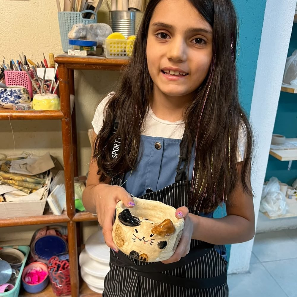 Niña mostrando su pieza de cerámica con forma de gato, esmaltada y terminada