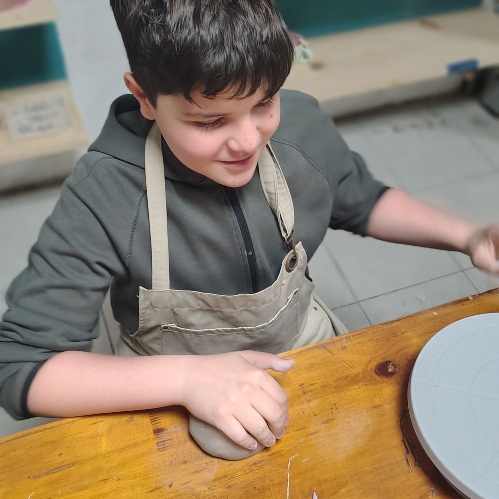 Niño sonriendo mientras modela arcilla en la clase de cerámica para niños