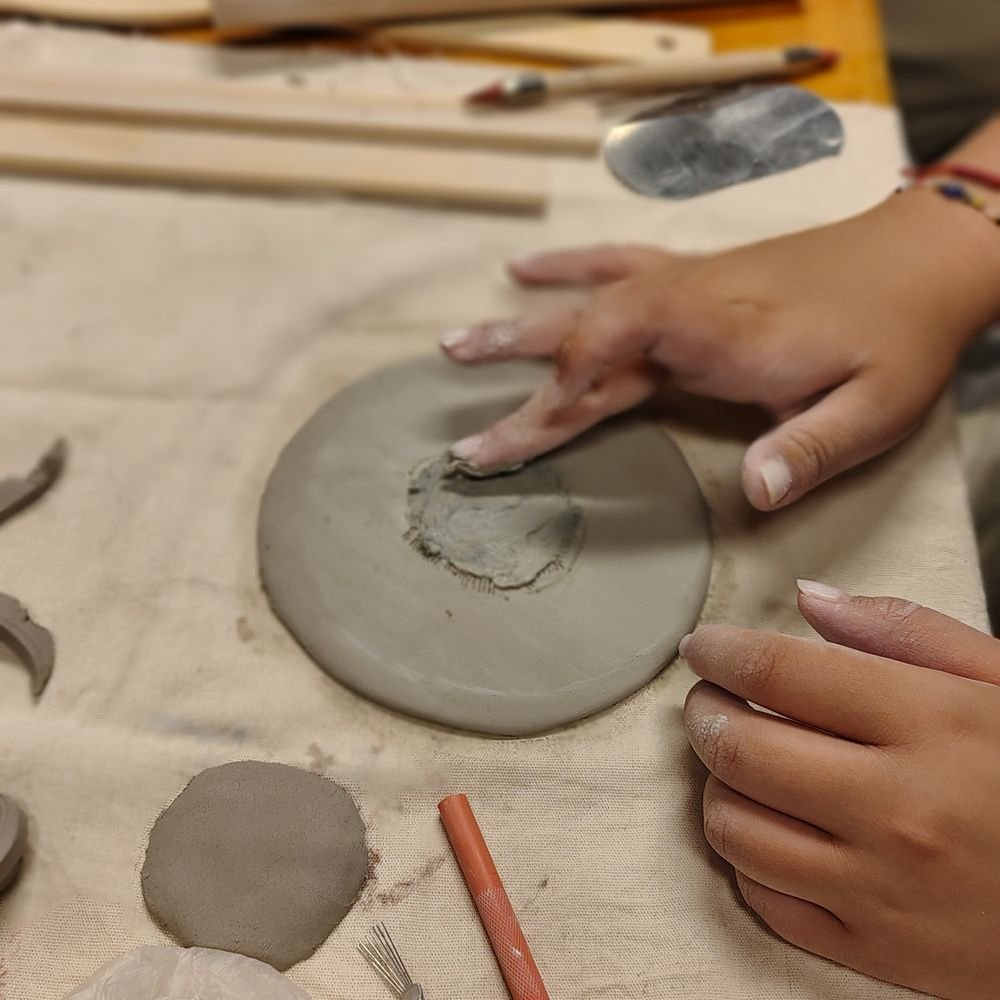Manos aplanando una placa de arcilla sobre un lienzo en clase de construcción manual