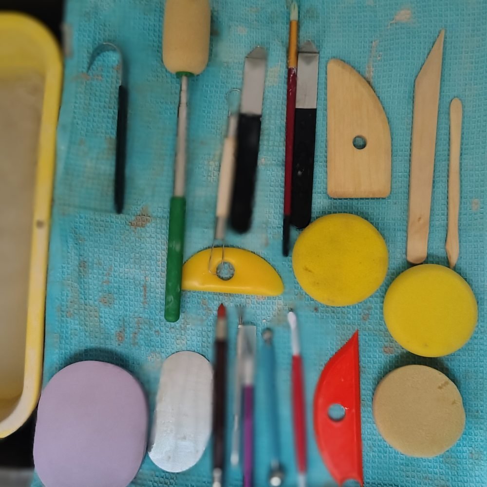 Herramientas para modelar cerámica acomodadas sobre la mesa: estecas, esponjas, cortadores y raspadores